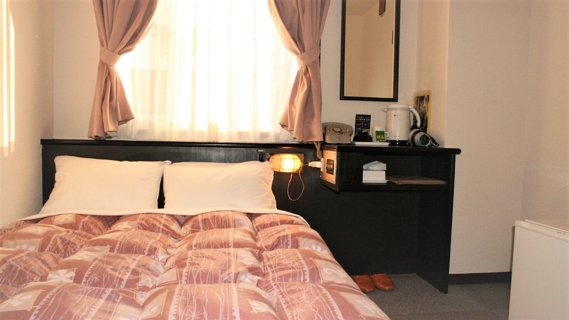 Une chambre d’hôtel avec un lit, une table de chevet avec une lampe, un miroir et une machine à café.
