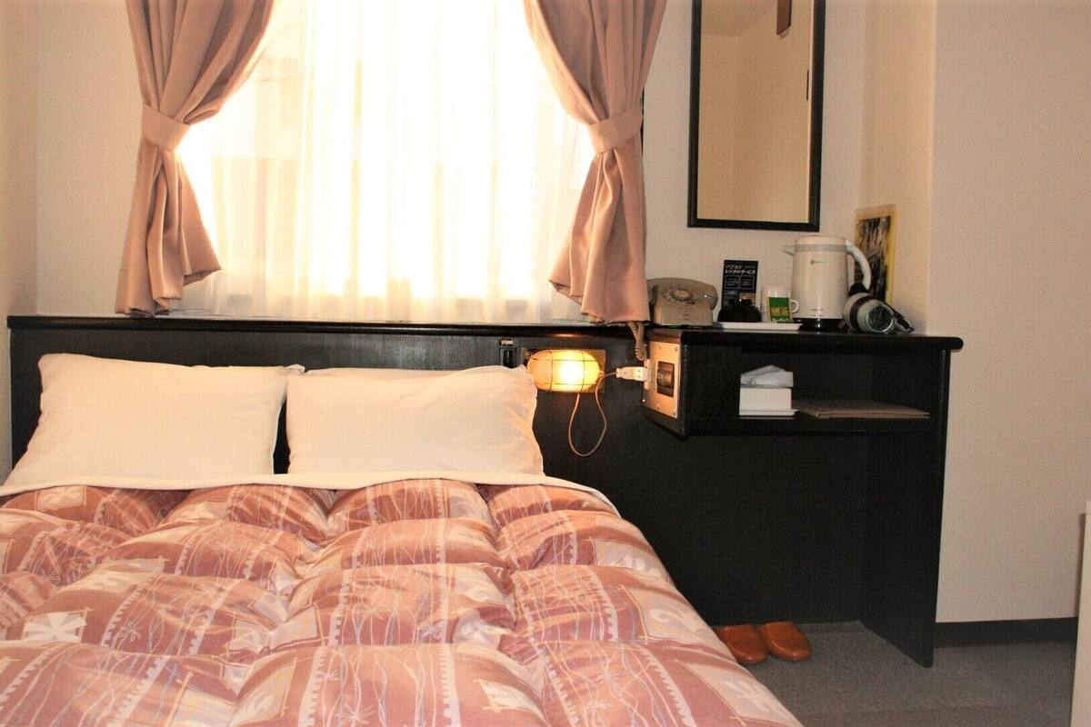 A hotel room with a bed, a bedside table with a lamp, a mirror, and a coffee machine.