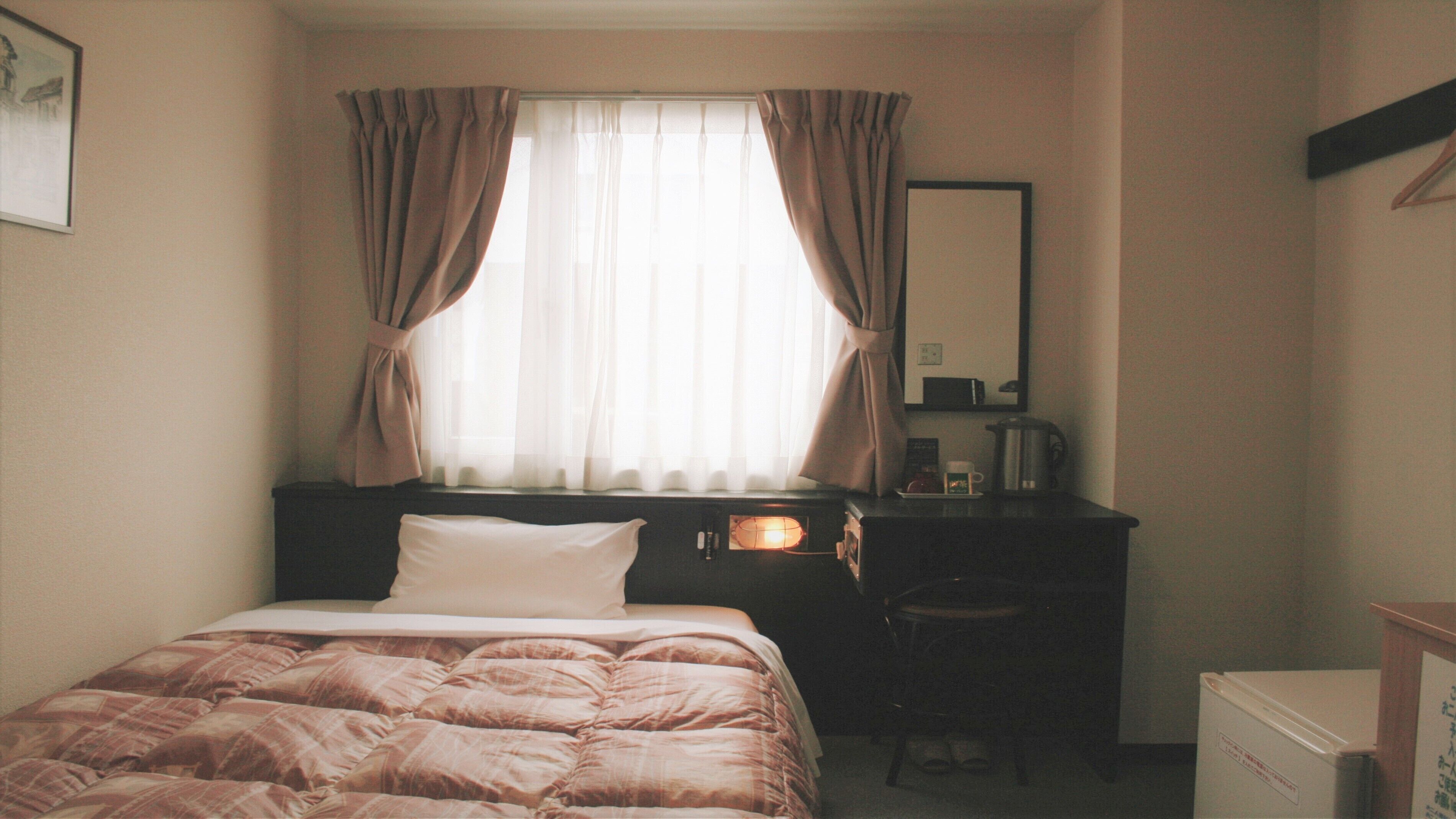 Une chambre d’hôtel avec un lit, un bureau avec une lampe, une chaise et un petit réfrigérateur.