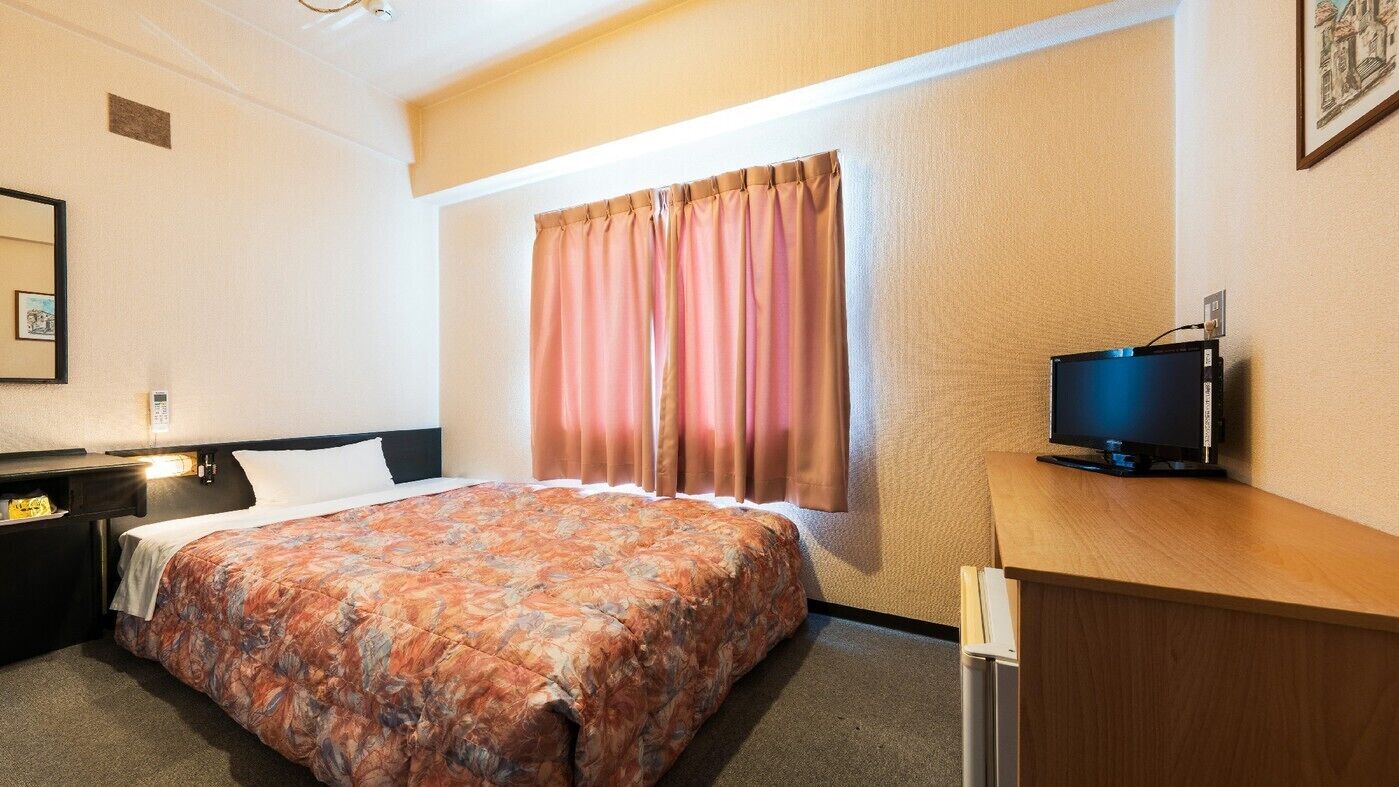Une chambre d’hôtel avec un lit, un bureau, une télévision et une fenêtre avec des rideaux.