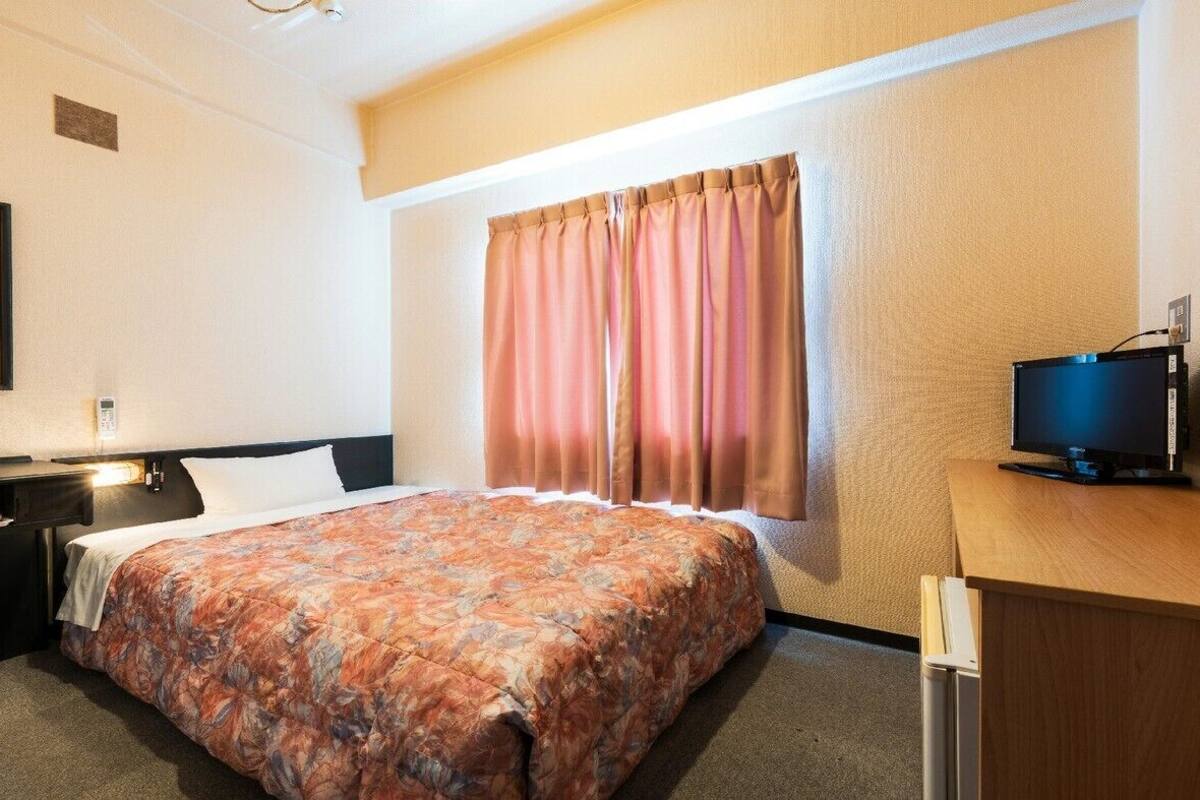 A hotel room with a bed, a desk, a television, and a window with curtains.