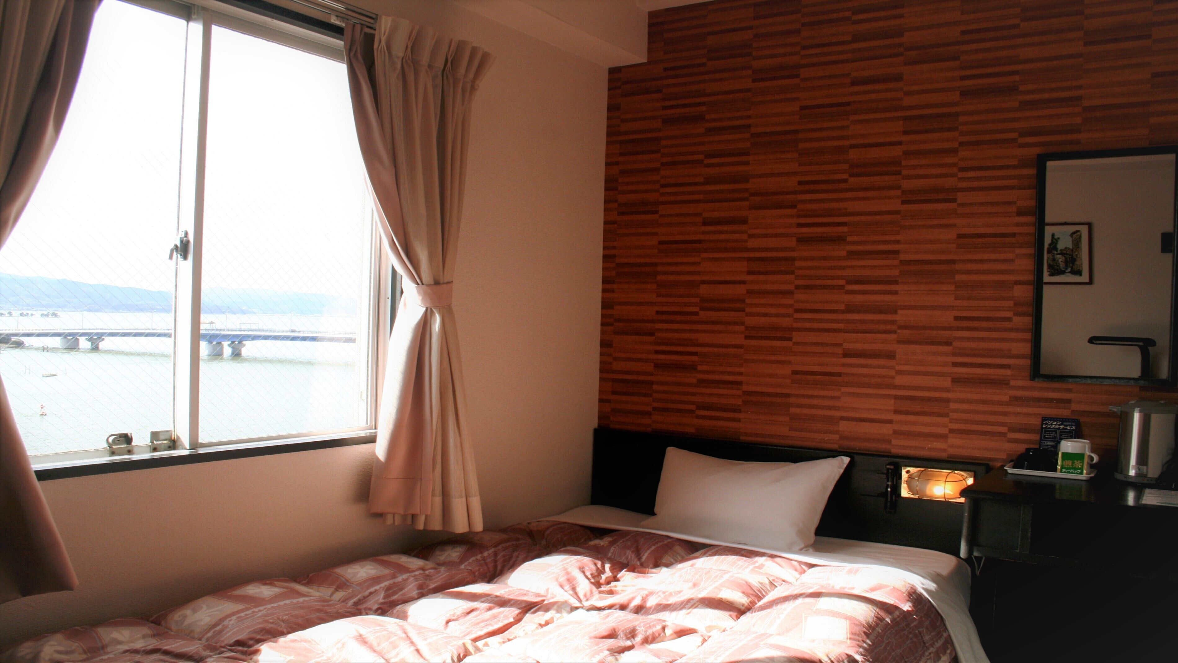 Une chambre d’hôtel avec un lit, une fenêtre avec des rideaux, un mur en bois, une table de chevet avec une lampe et une vue sur un pont.