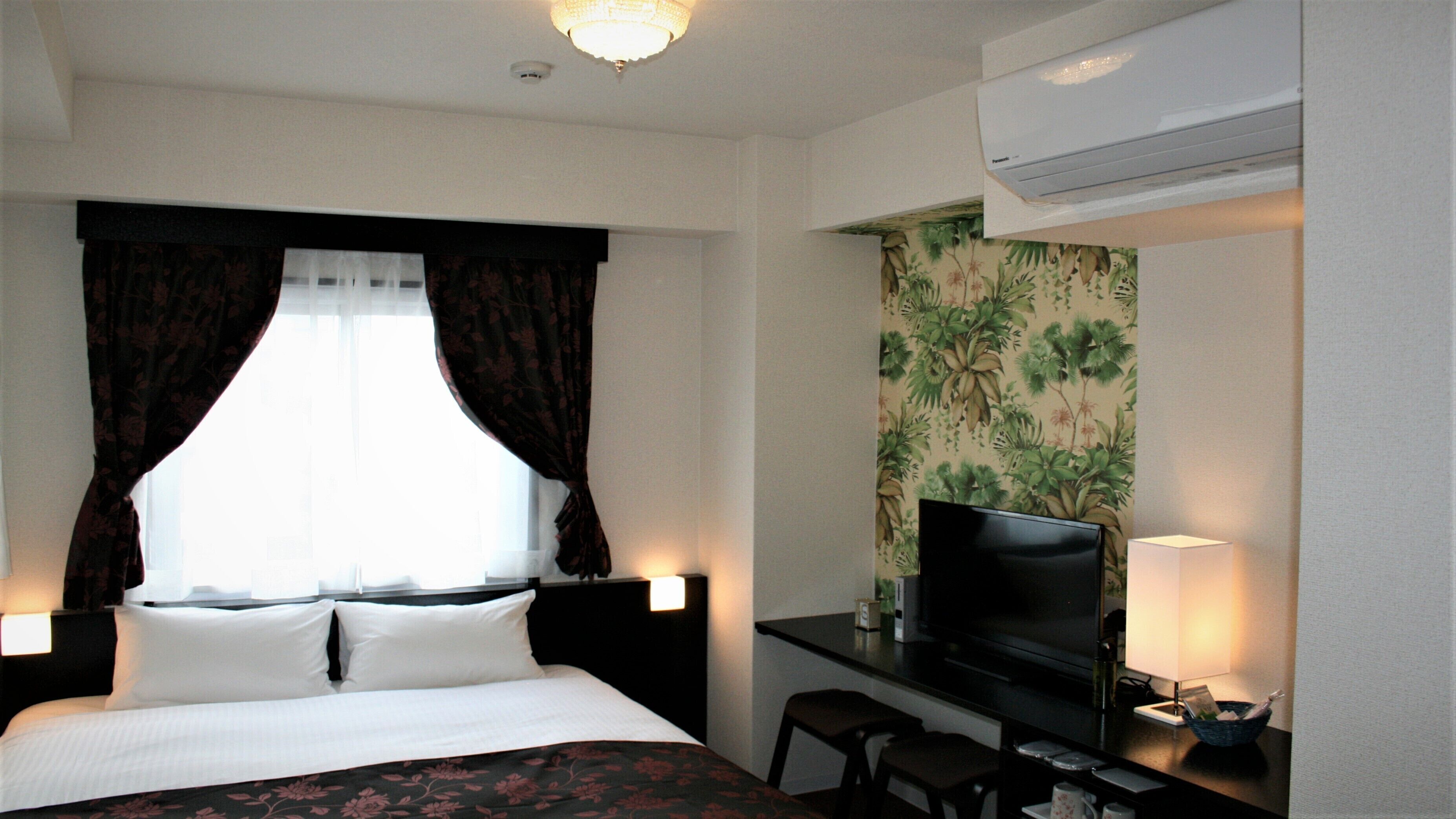 Une chambre d’hôtel équipée d’un lit, d’un bureau avec une télévision, d’une chaise et d’un appareil de climatisation.