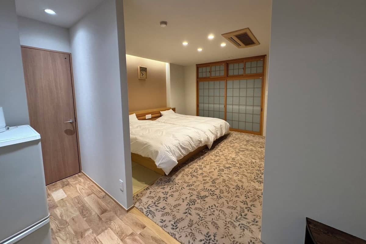 A bedroom with a bed, a wooden wardrobe, a small table, and a patterned rug.