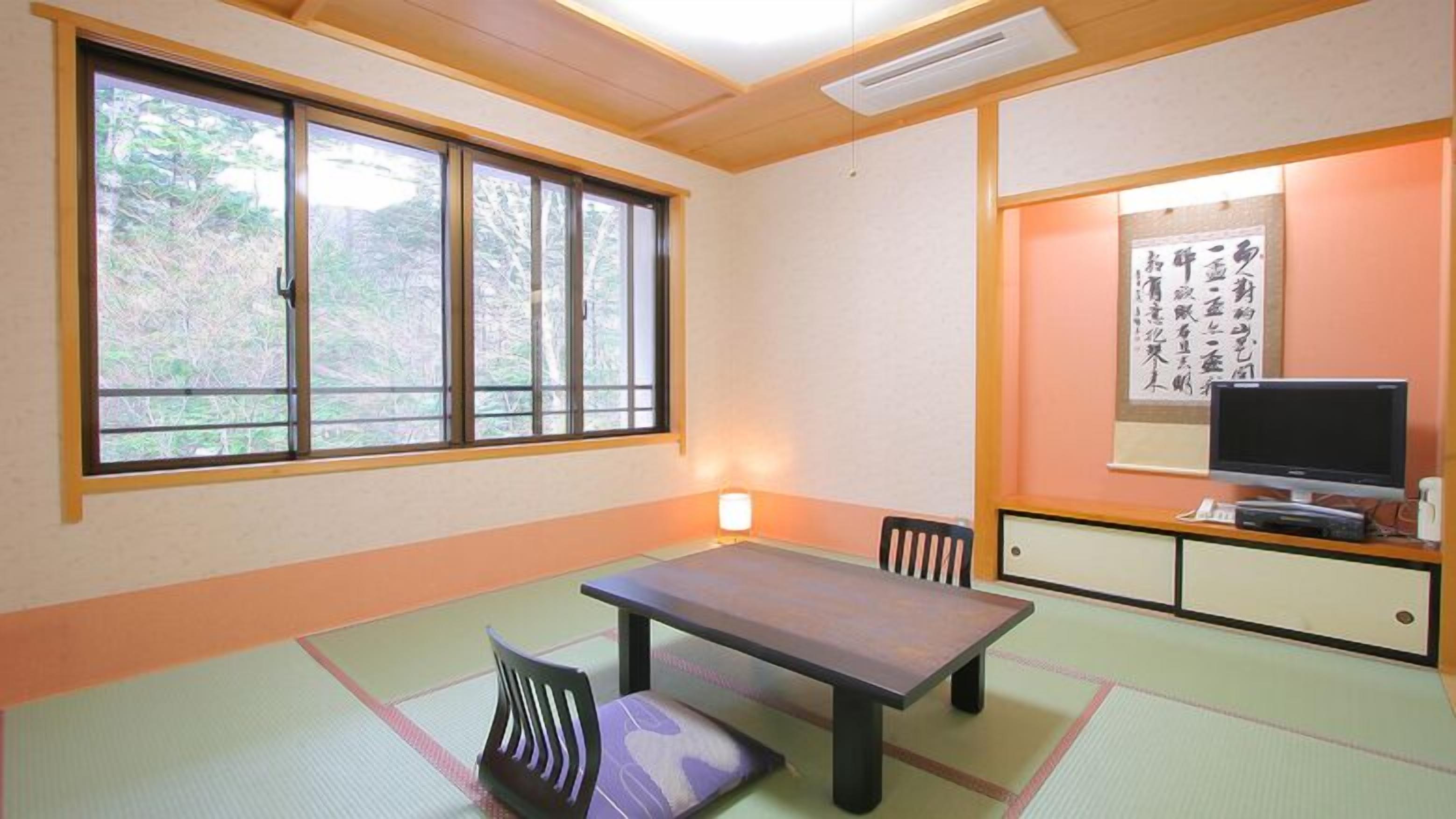 Una habitación tradicional japonesa con suelo de tatami, una mesa baja, un televisor y una obra de caligrafía en la pared.