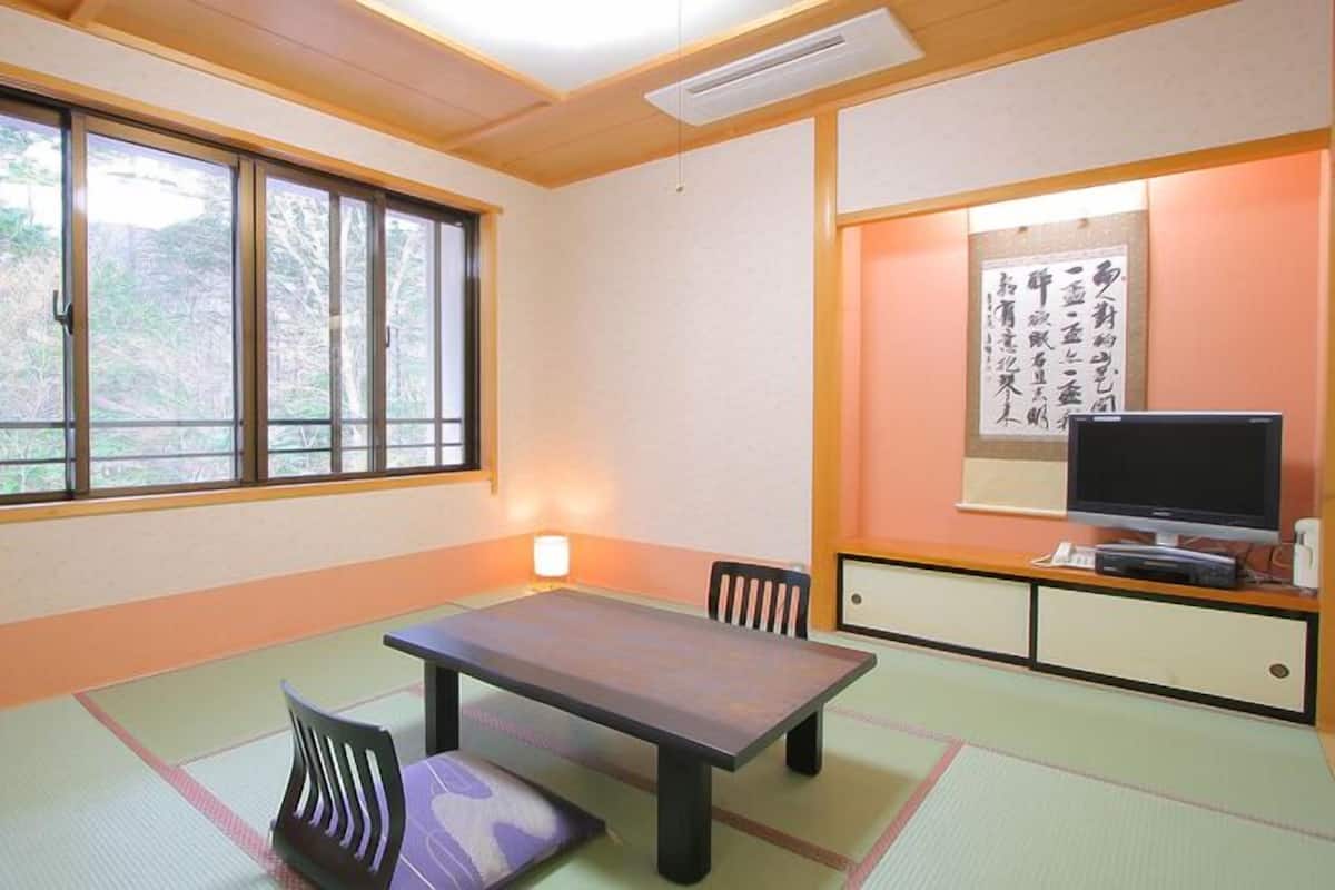 A traditional Japanese room with tatami flooring, a low table, a television, and a calligraphy piece on the wall.