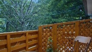 A wooden deck with a table and a rocking chair, surrounded by a wooden fence and trees. - Hirayu Onsen KKR Hirayu Takaraso (Takayama)