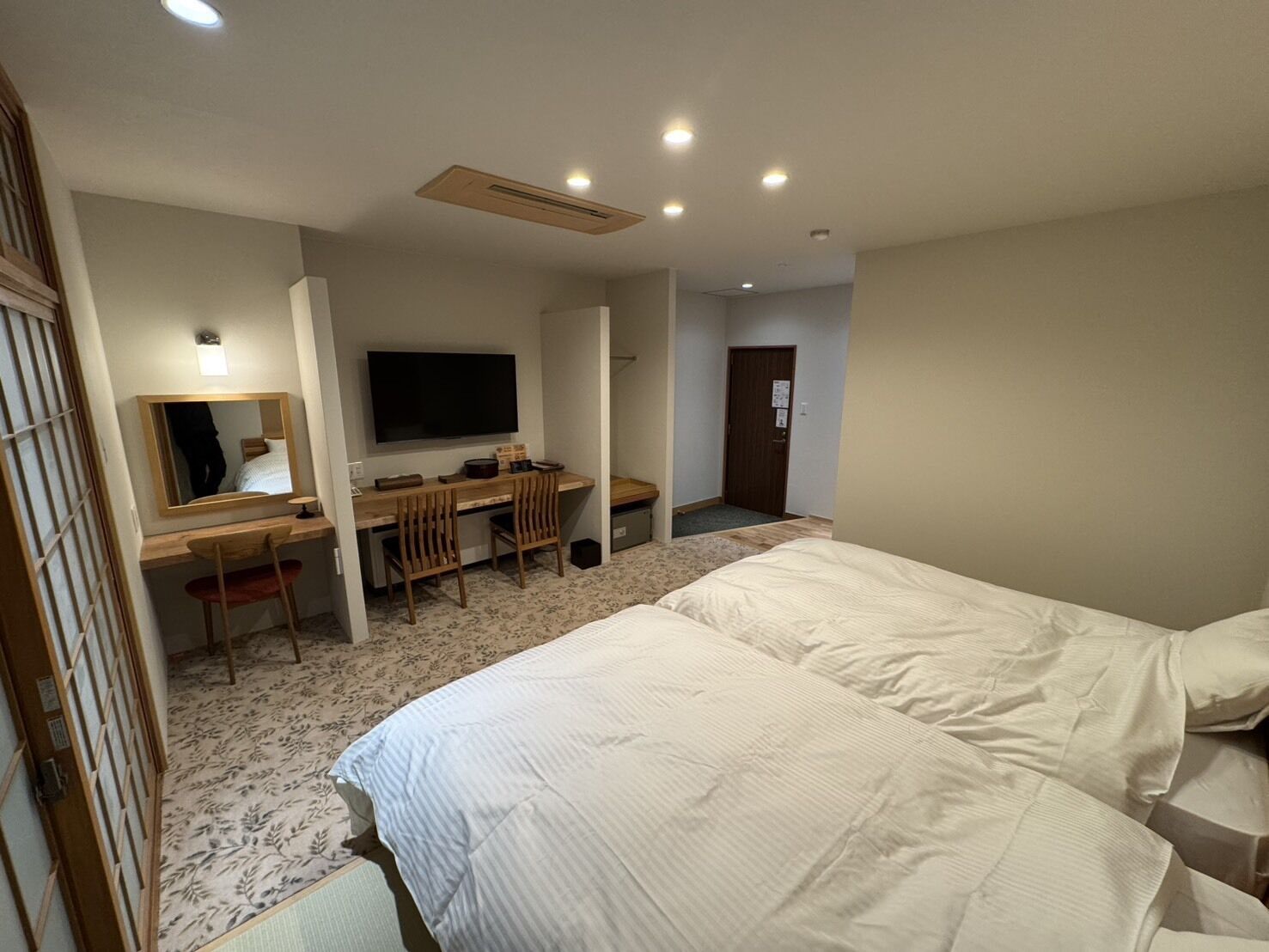 Habitación de hotel con dos camas, un escritorio con silla, un televisor y un espejo.