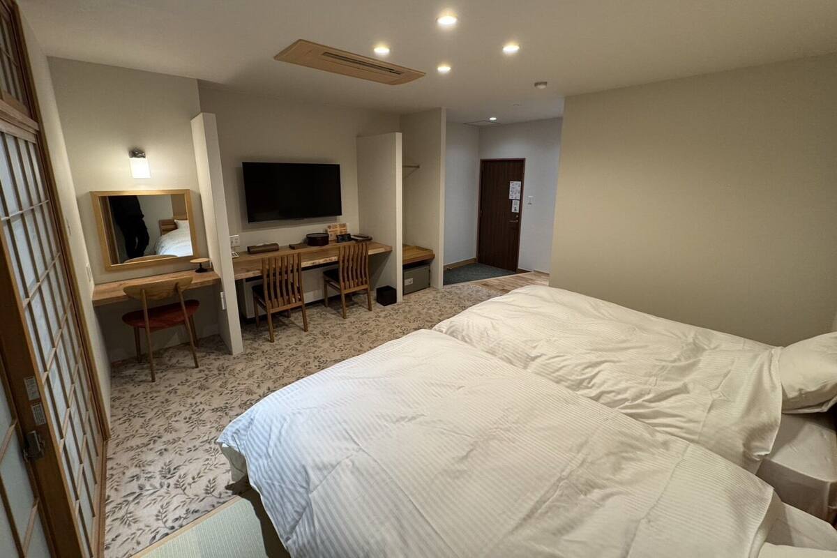 A hotel room with two beds, a desk with a chair, a television, and a mirror.