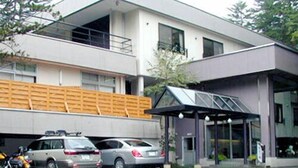 A modern building with a covered entrance, outdoor seating, and parked cars. - Hirayu Onsen KKR Hirayu Takaraso (Takayama)