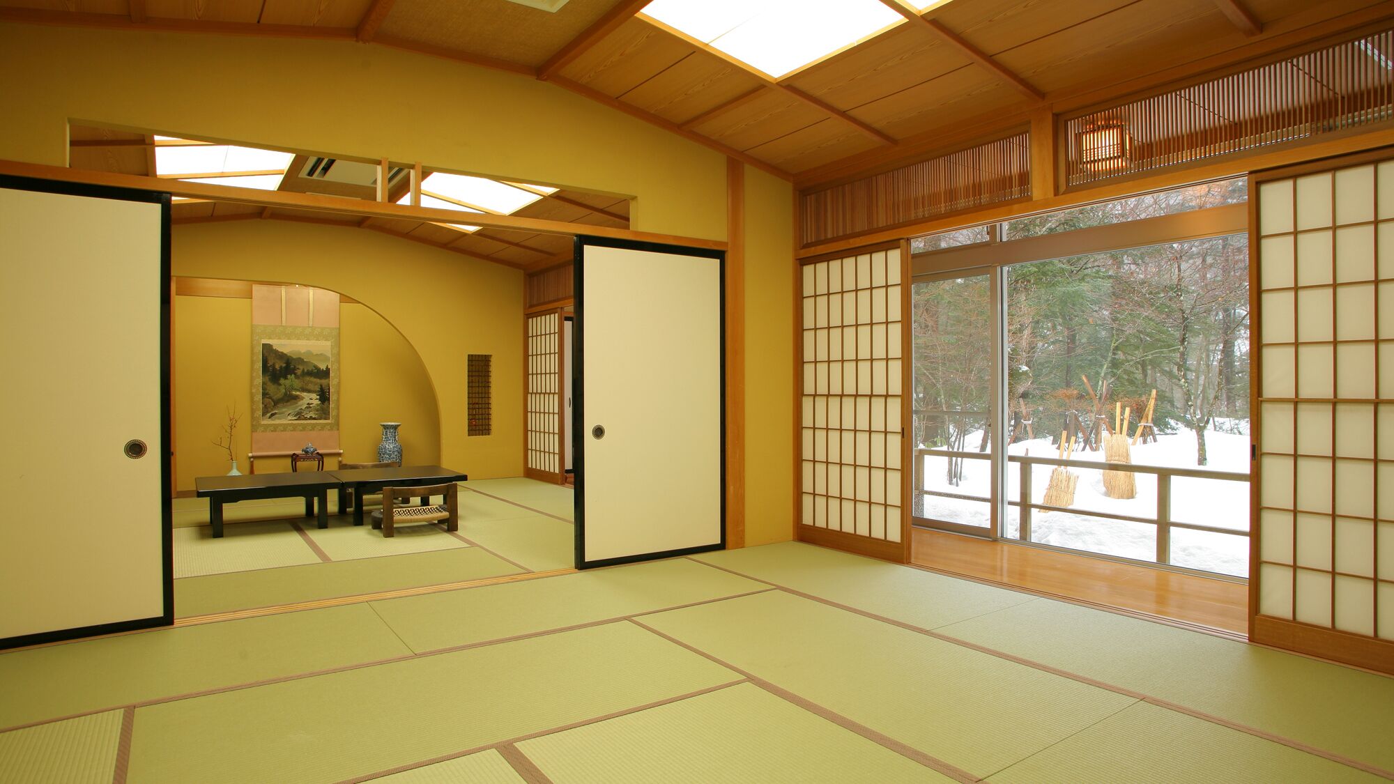 Una habitación japonesa tradicional con suelo de tatami, puertas correderas y vistas a un paisaje nevado.