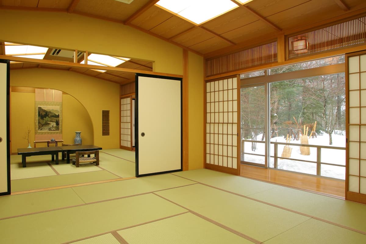 A traditional Japanese room with tatami flooring, sliding doors, and a view of a snowy landscape.