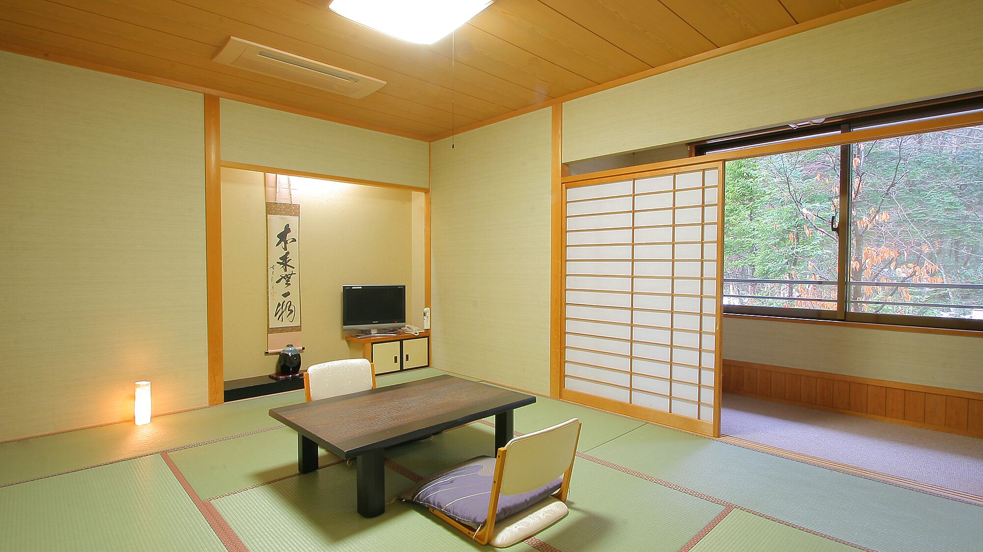 Una habitación japonesa tradicional con suelo de tatami, una mesa baja, un televisor y un fusuma corredero.