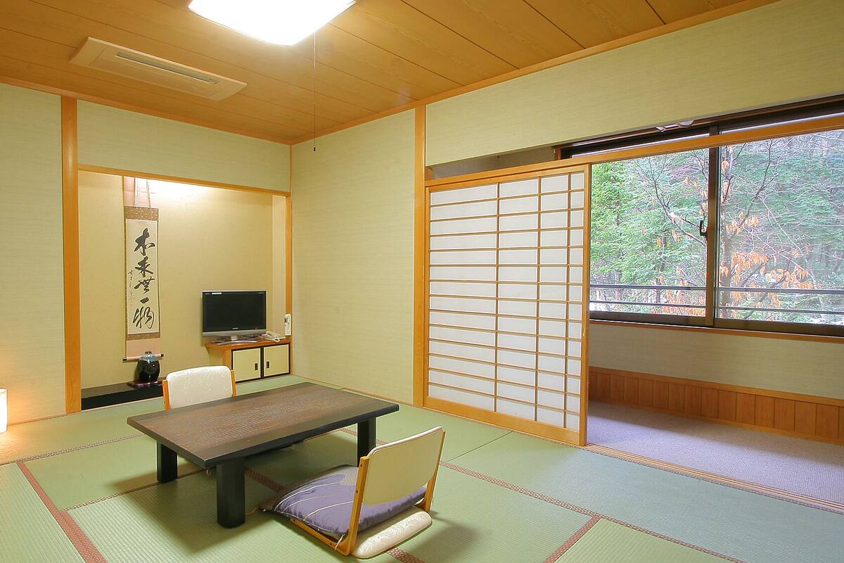 A traditional Japanese room with tatami flooring, a low table, a television, and a sliding shoji screen.