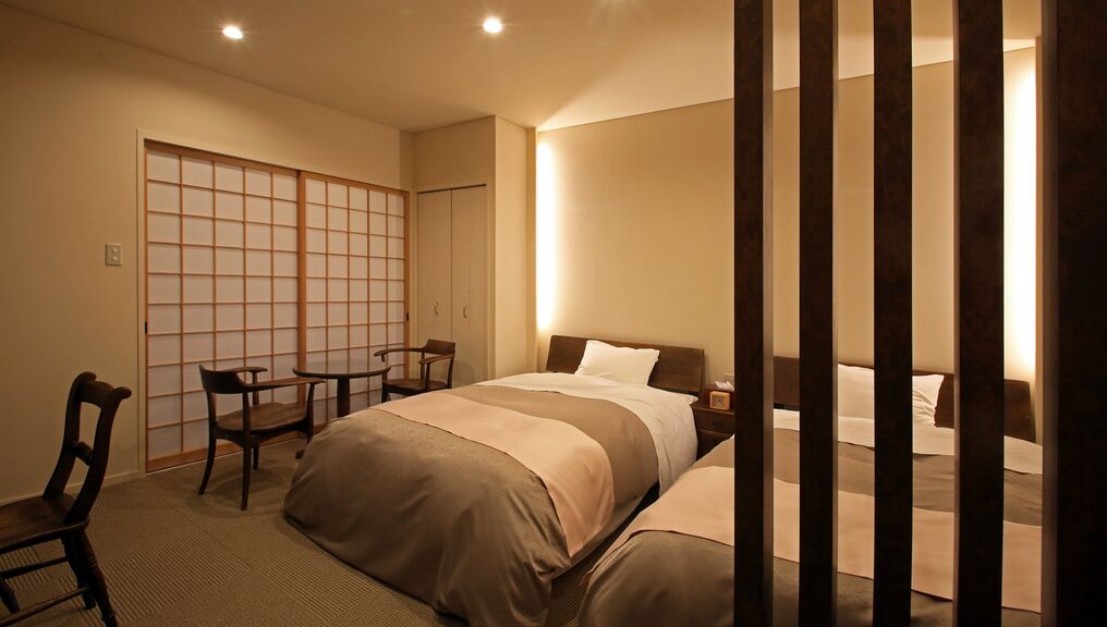 Habitación de hotel con cama, mesitas de noche, una silla, un escritorio y un panel corredero tipo shoji.