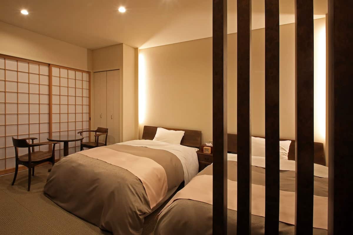 A hotel room with a bed, bedside table, chair, and a sliding shoji screen.