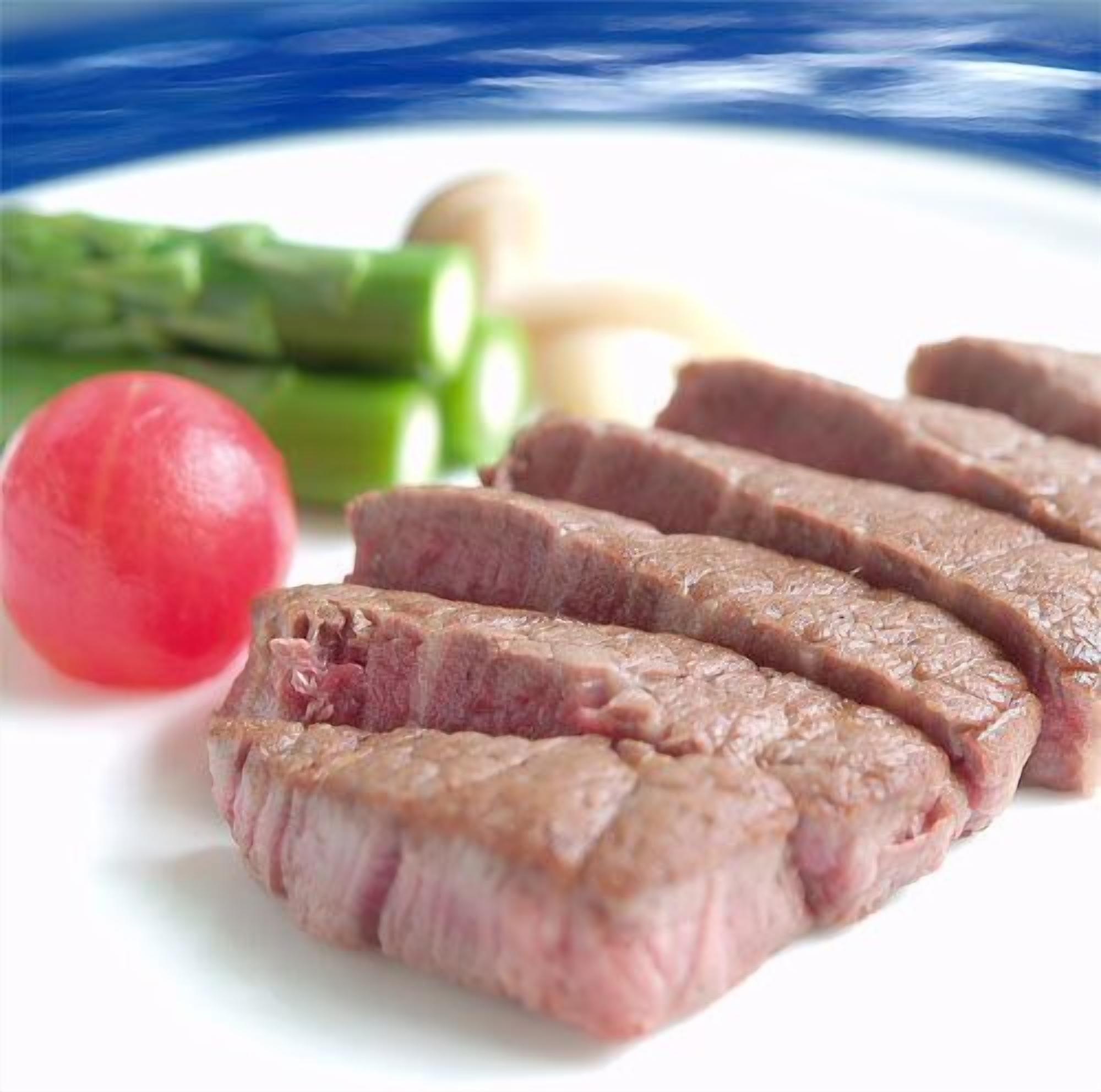 A plate with sliced meat, green vegetables, and a red fruit.
