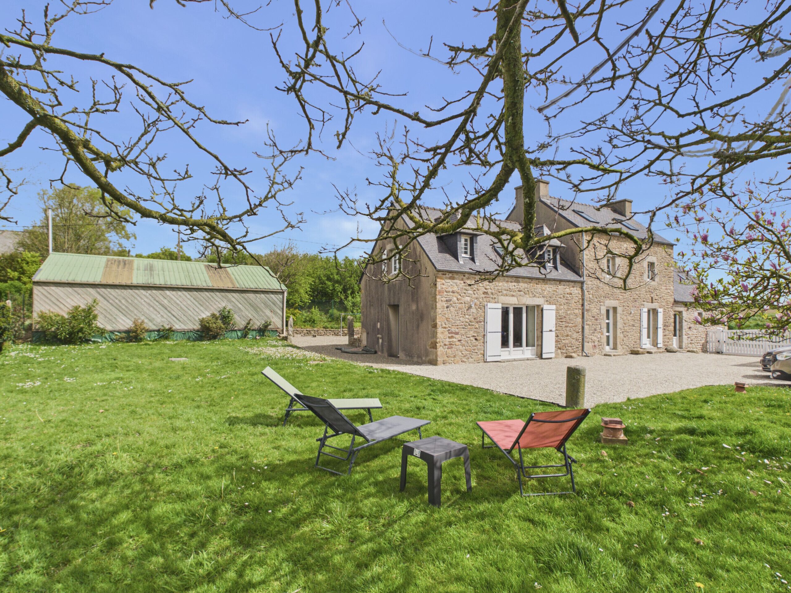 A stone house with a large lawn, two lounge chairs, and a table.