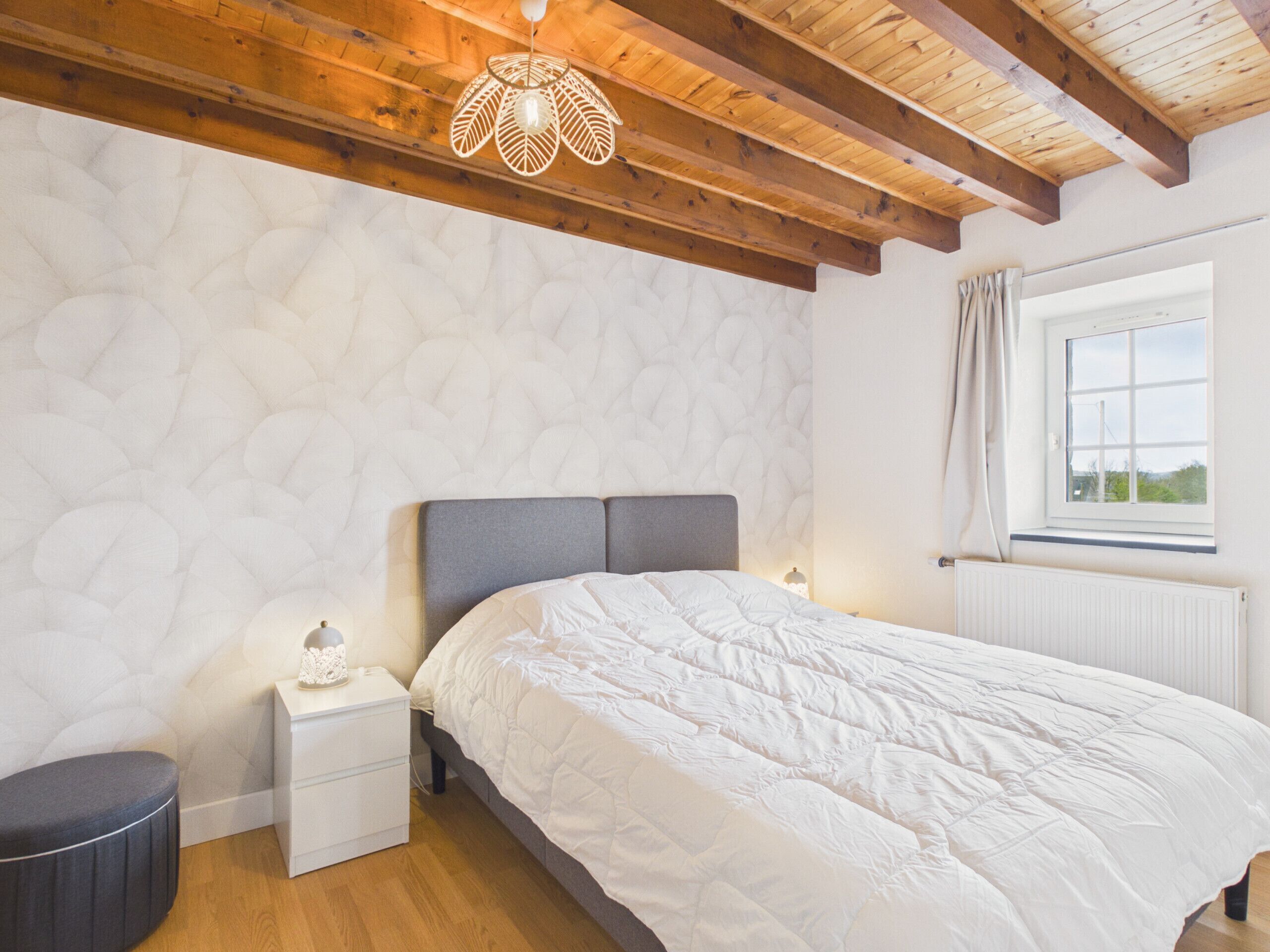 A bedroom with a bed, nightstand, and a window with curtains.