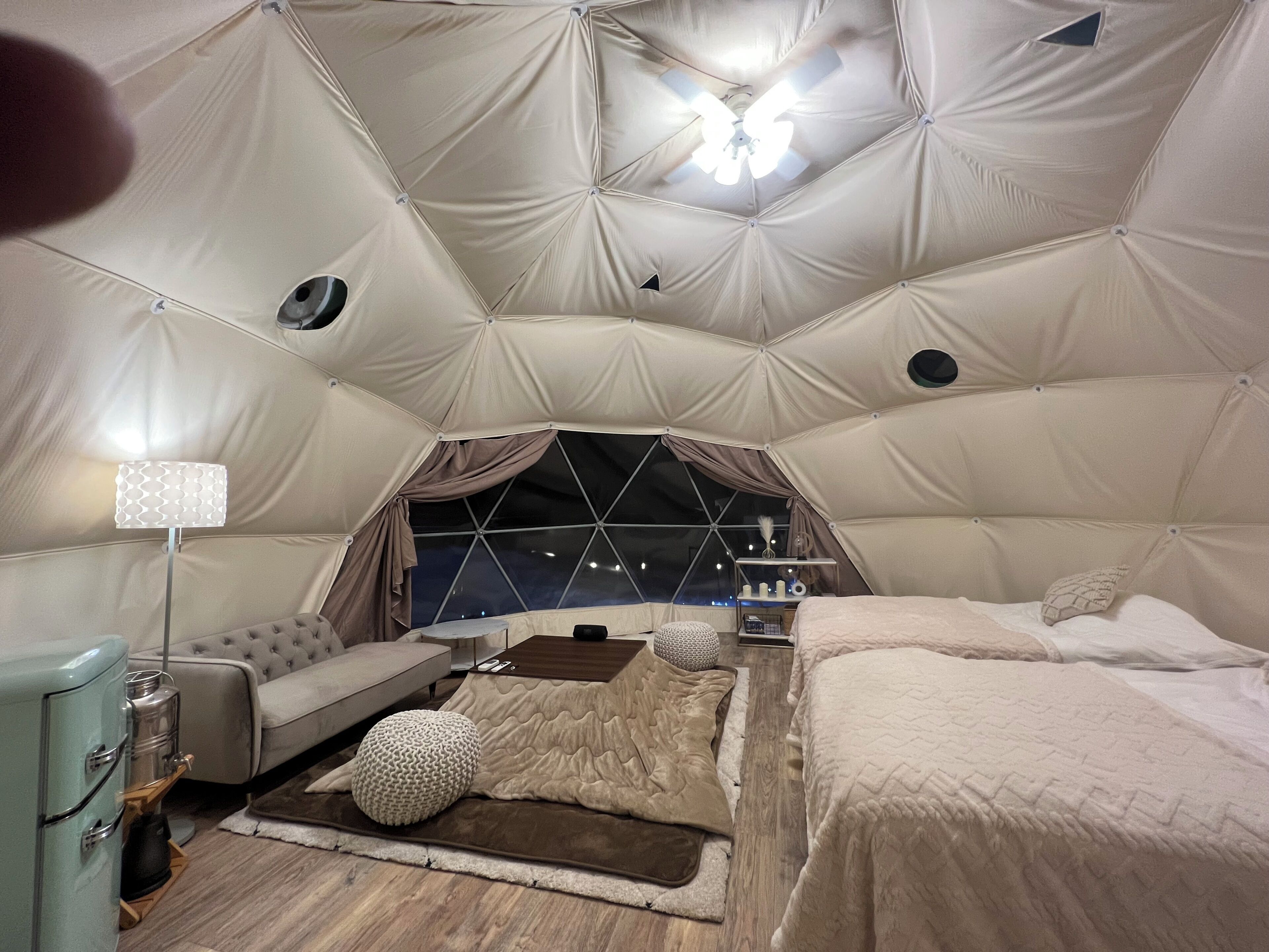 Uma sala no estilo de tenda, com cama, área de estar e uma luminária.