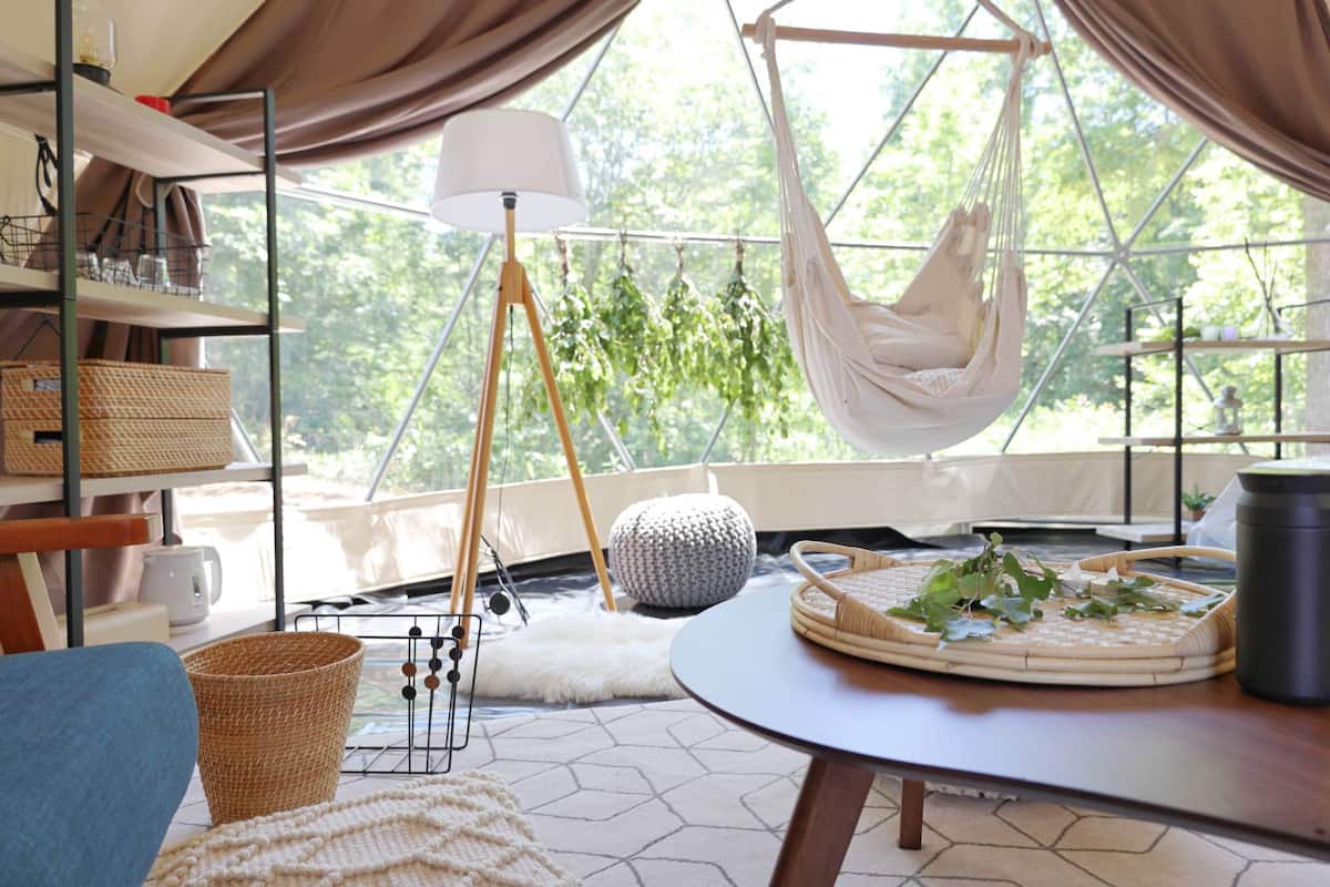 A hammock, a round table, a lamp, and a view of trees through large windows.