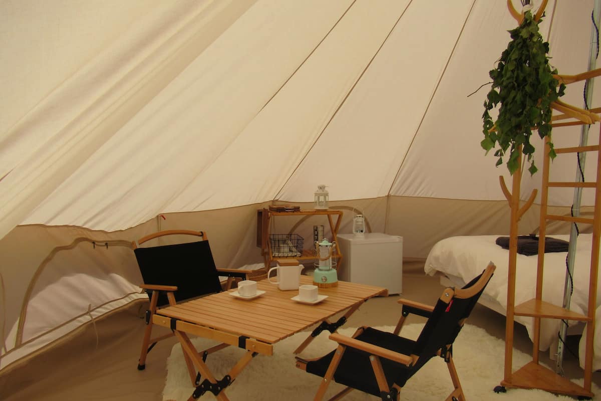 Uma tenda com uma mesa, cadeiras, uma planta pendente e um candeeiro.