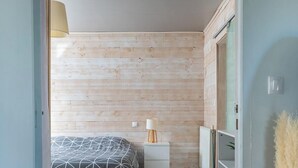 Un dormitorio con pared de madera, una cama con colcha de estampado geométrico, una mesita de noche con lámpara y un armario.