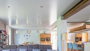 Amplia sala de estar con un sofá, una estantería y una cocina visible a través de una puerta abierta.