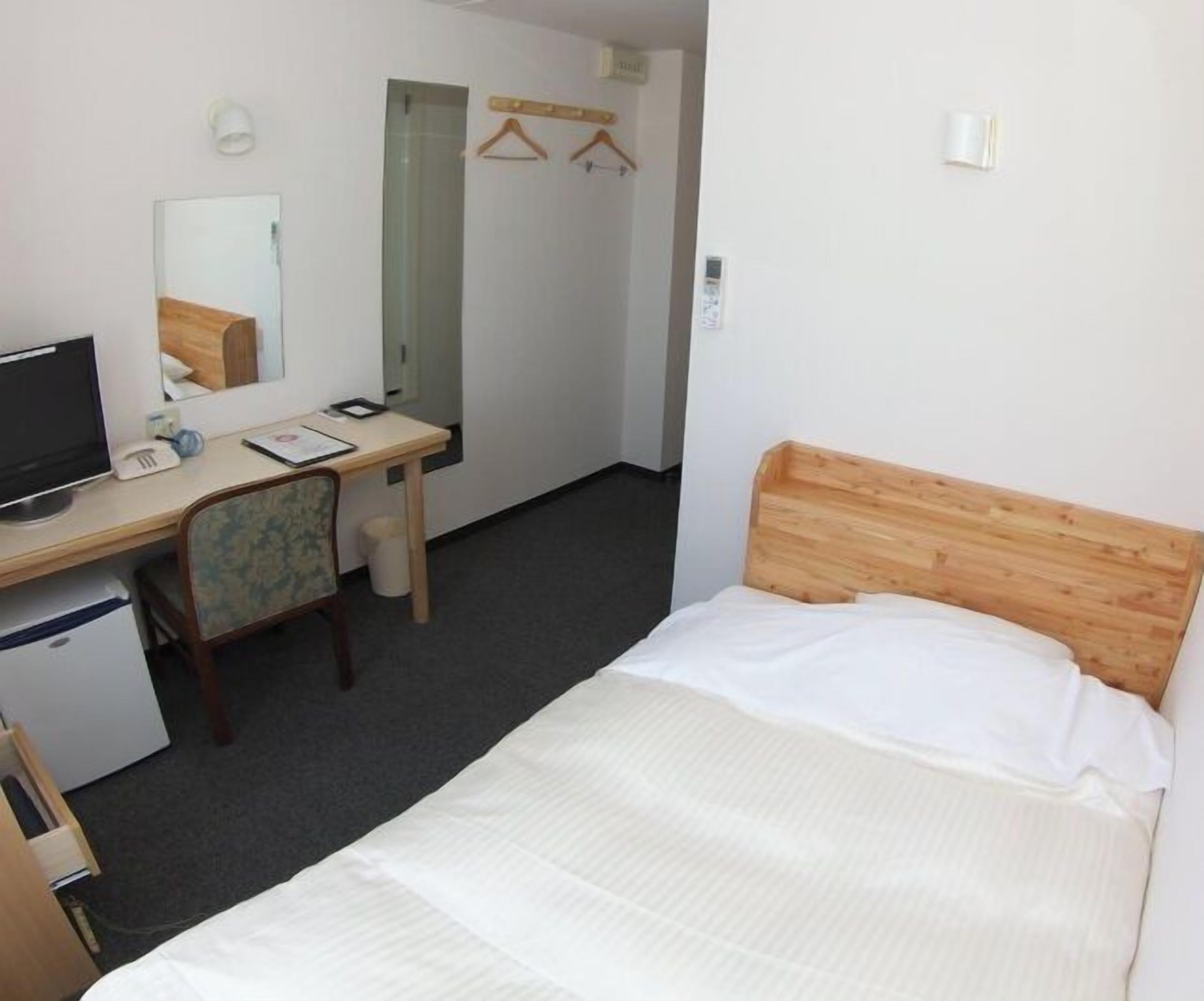 Una camera d'albergo con un letto, una scrivania, una sedia e uno specchio.