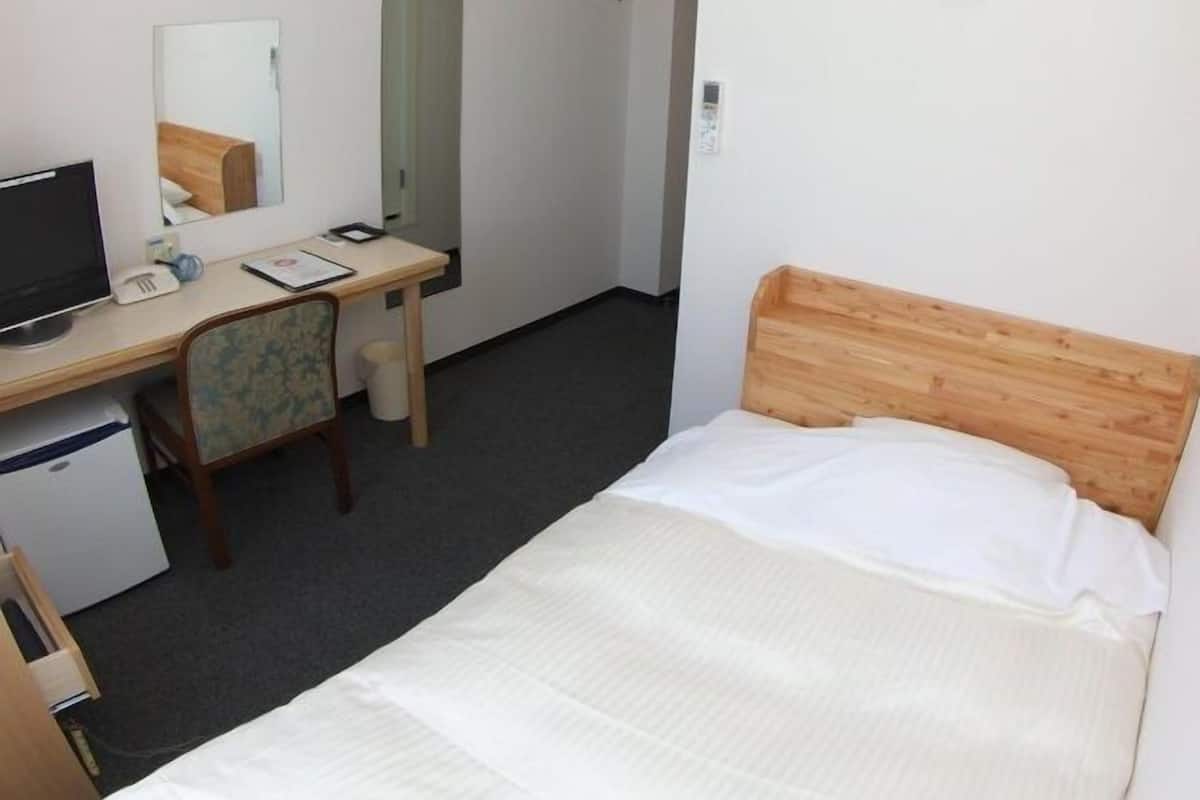 Une chambre d’hôtel comprenant un lit, un bureau avec un ordinateur, une chaise, un miroir et une armoire.