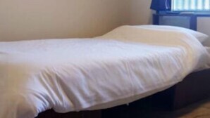 Un lit simple dans une chambre avec une fenêtre, un rideau et un climatiseur fixé au mur.