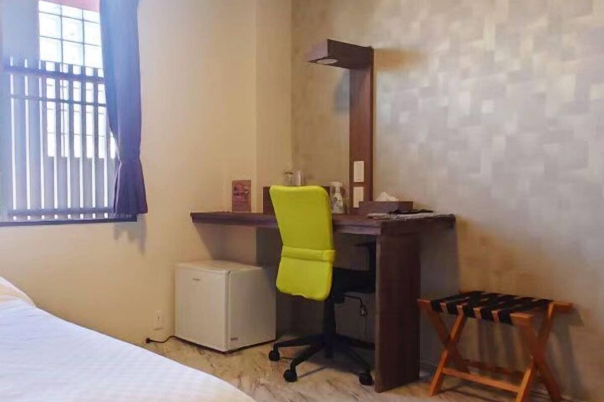Une chambre d’hôtel comprenant un lit, un bureau avec une chaise, un petit réfrigérateur et une fenêtre avec des rideaux.