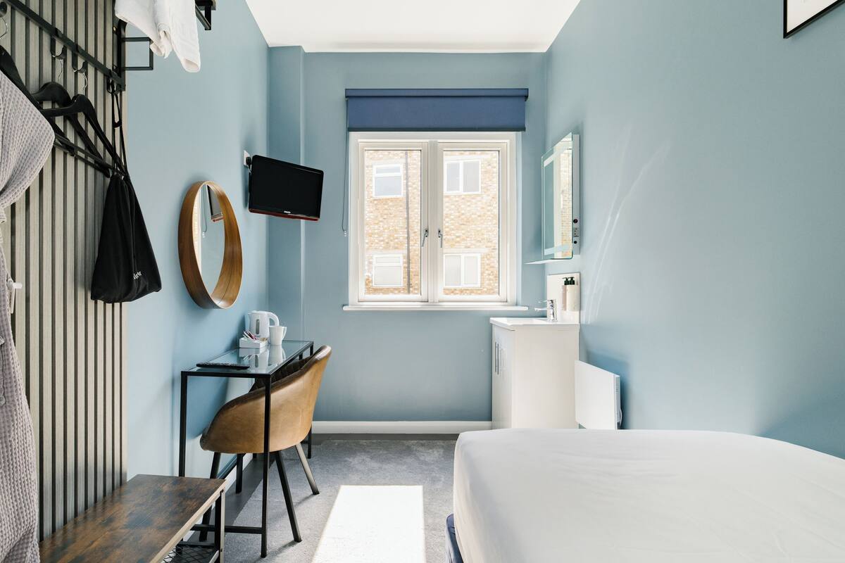 A hotel room with a bed, a desk with a chair, a television, a window, and a bathroom.