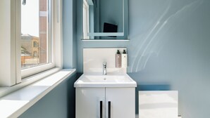 A bathroom with a window, a sink, a mirror, and a cabinet.