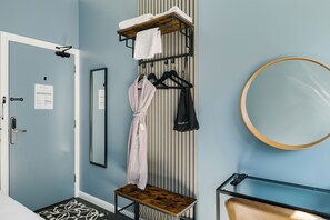 A hotel room with a wooden bench, a mirror, a coat rack with towels and a robe, and a door with a sign. - Borough High Street Rooms (London)