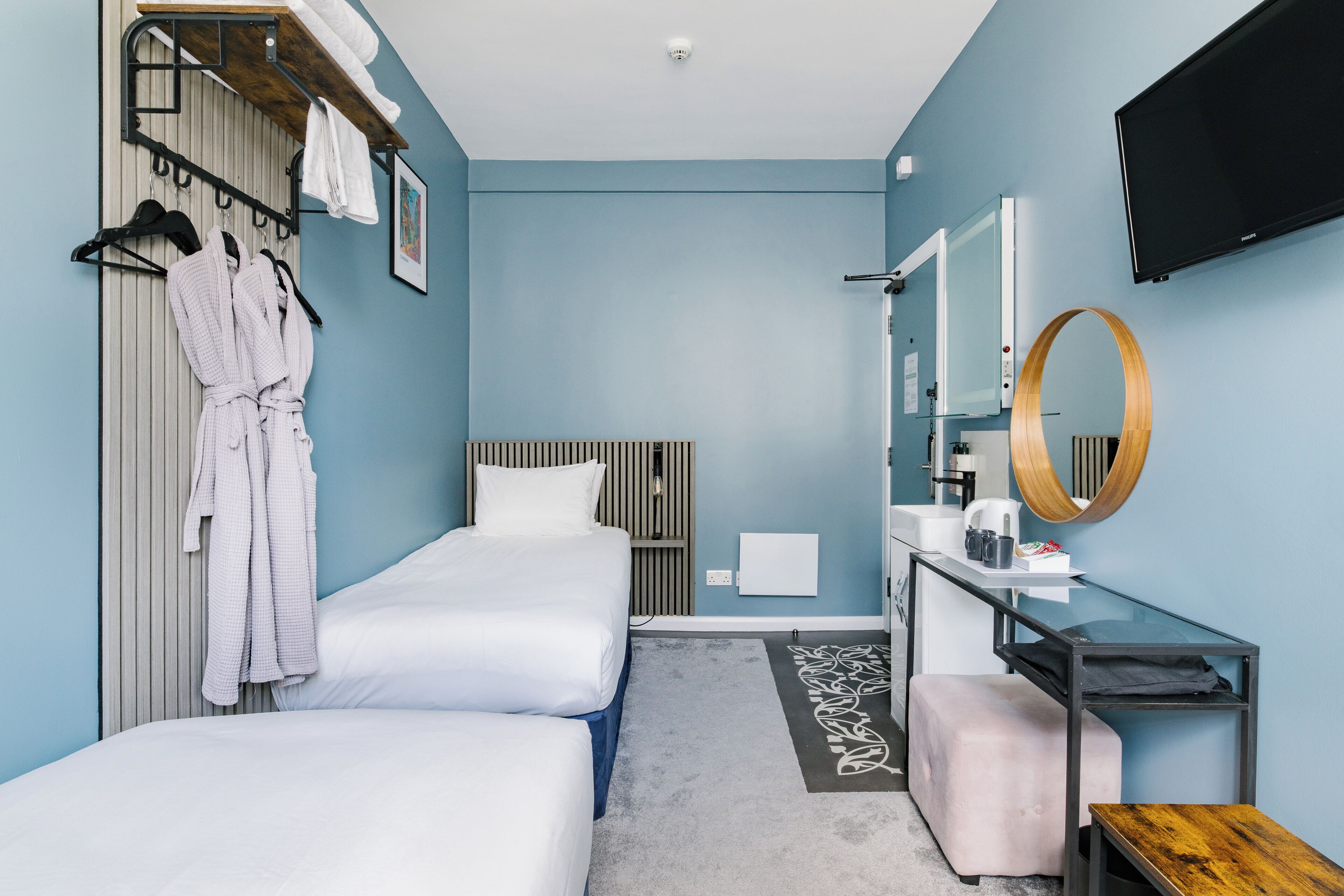 Une chambre d’hôtel avec deux lits, un bureau avec un miroir, une télévision et un banc en bois.