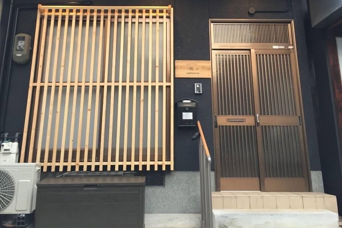 A two-story building with a dark facade, a wooden slatted entrance, and a metal door.