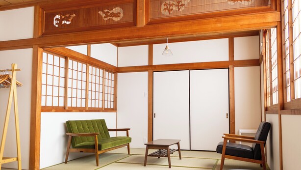 A traditional Japanese room with tatami flooring, a green sofa, a black chair, and a small table.