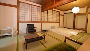 A traditional Japanese room with tatami flooring, a futon bed, a black leather chair, a small table, and a white shelf.