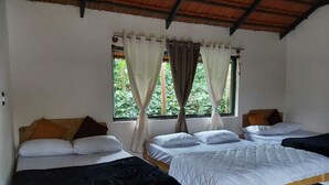 A room with four single beds, a wooden ceiling, and a window with curtains.