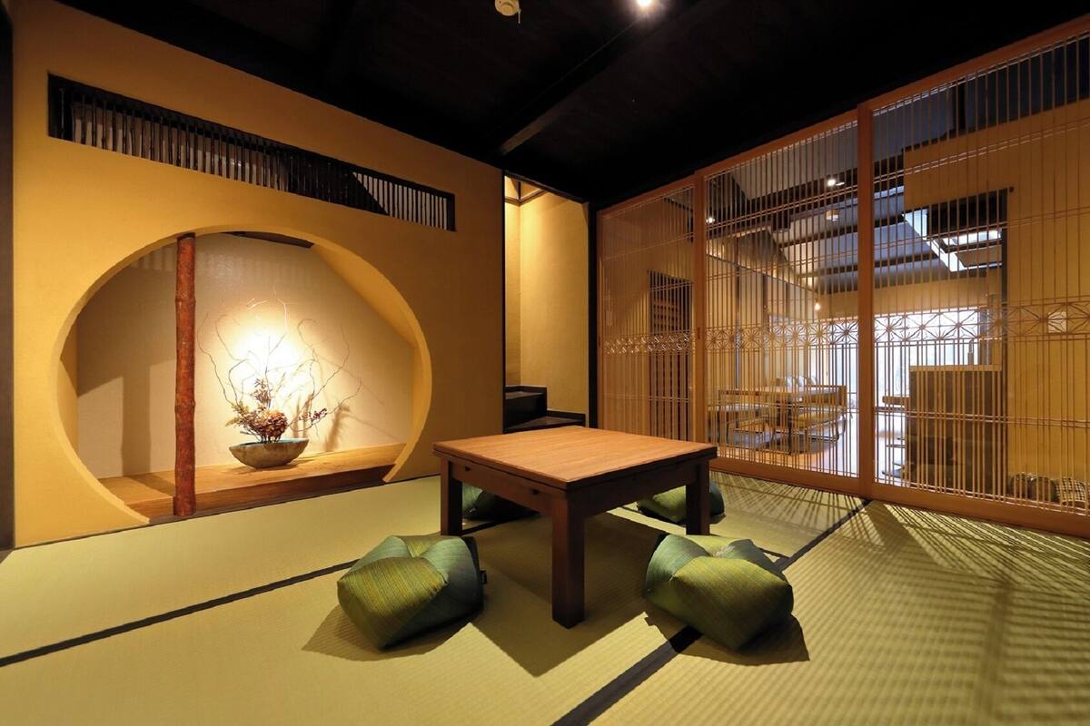 Ein traditioneller japanischer Raum mit Tatami-Bodenbelag, einem niedrigen Tisch, Kissen und einem Shoji-Bildschirm.