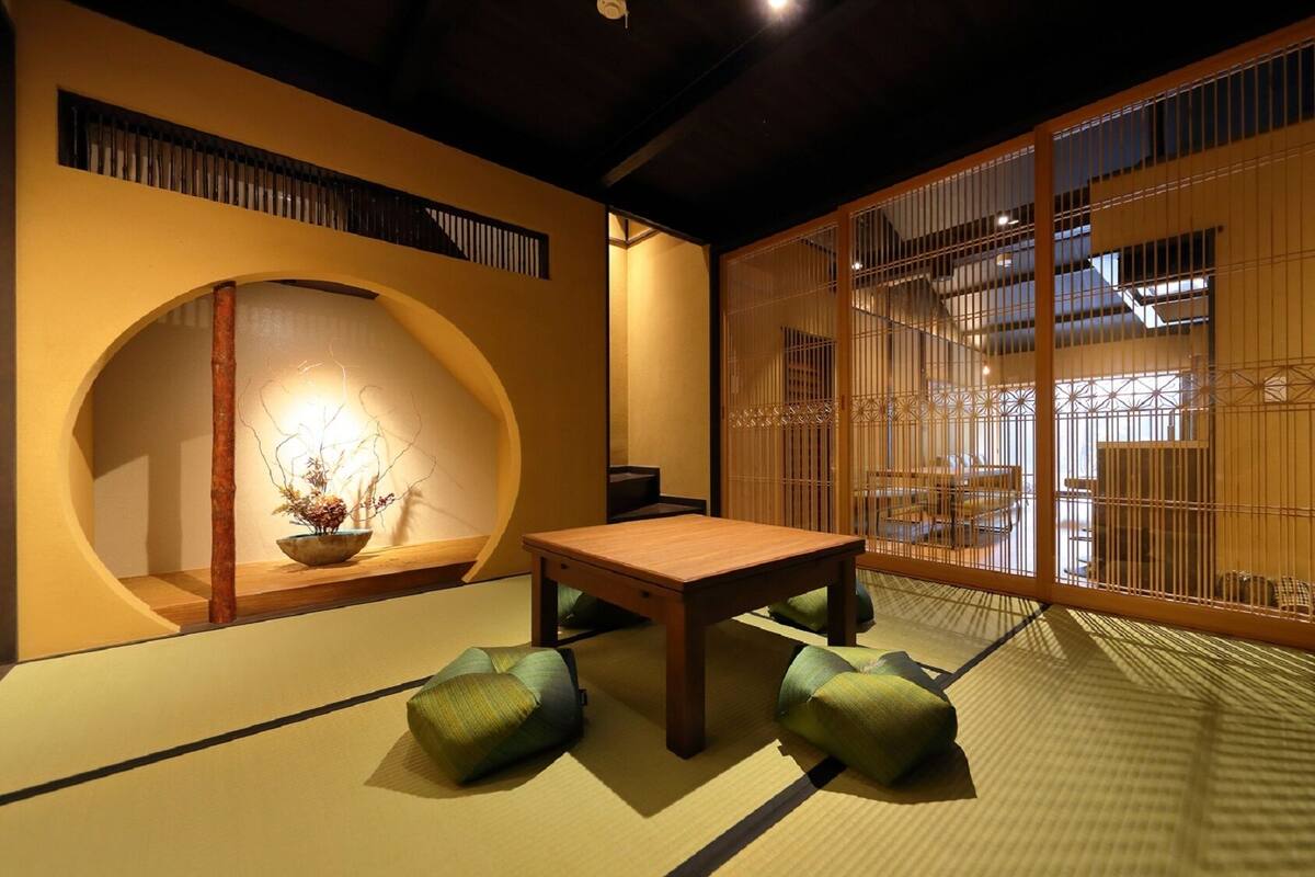 Ein traditioneller japanischer Raum mit Tatami-Boden, einem niedrigen Tisch, Kissen, einem Shoji-Bildschirm und einer Wandrolle.