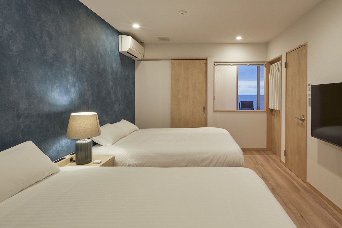 A hotel room with two beds, a TV, a window with a view, and an air conditioning unit.