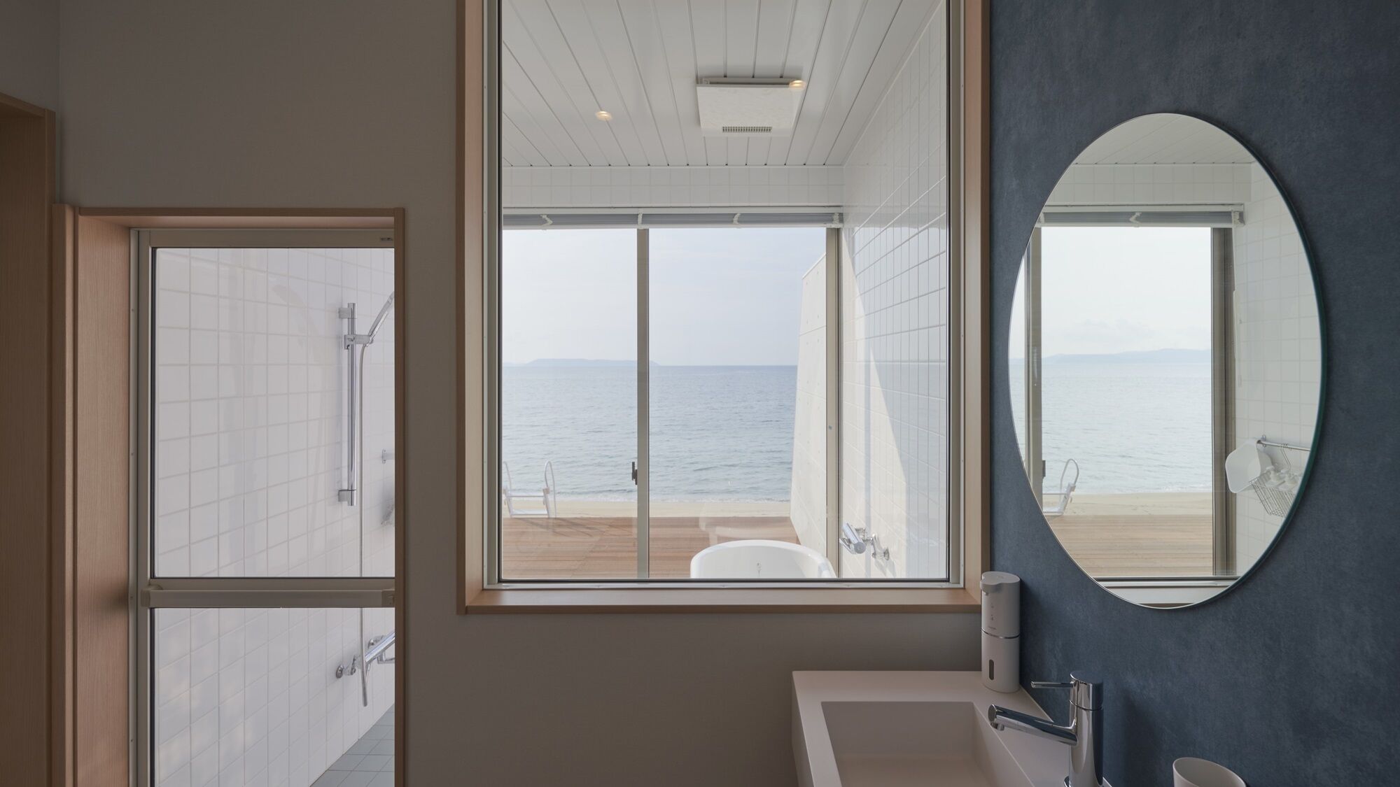Ein Badezimmer mit großem Fenster, einem runden Spiegel und Meerblick.