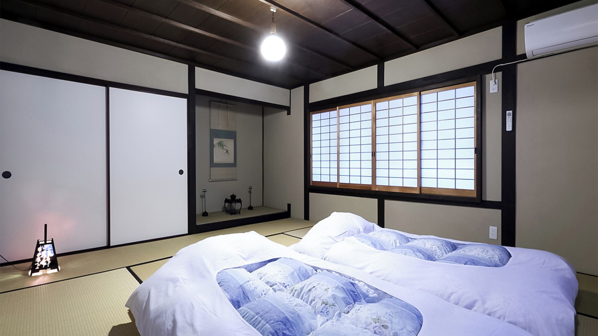 Perinteinen japanilaistyylinen huone, jossa on tatamimatto, futon-patja, liukuovet ja shoji-paperi-ikkuna.