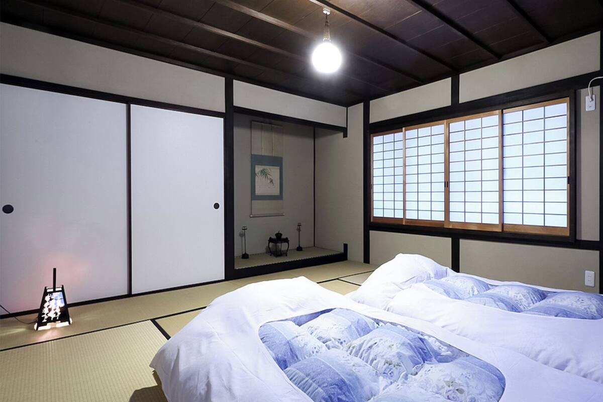 A traditional Japanese-style room with tatami flooring, a futon bed, sliding doors, and a shoji screen window.
