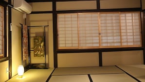 A traditional Japanese room with tatami flooring, a shoji screen, a hanging scroll, and a wall-mounted air conditioner. - Kyomachiya Oyado Hana (Kyoto)