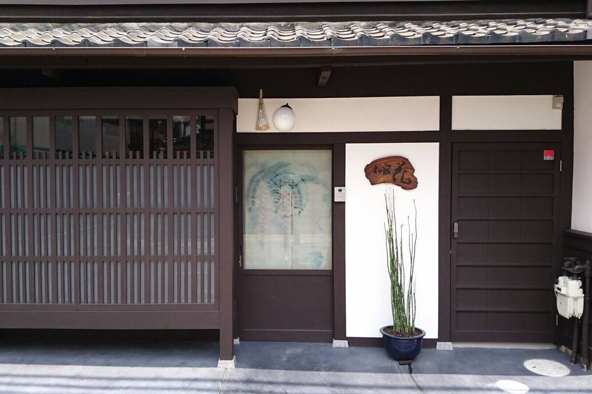 A traditional Japanese building with a sliding door, a small potted plant, and a wooden plaque with Japanese characters.