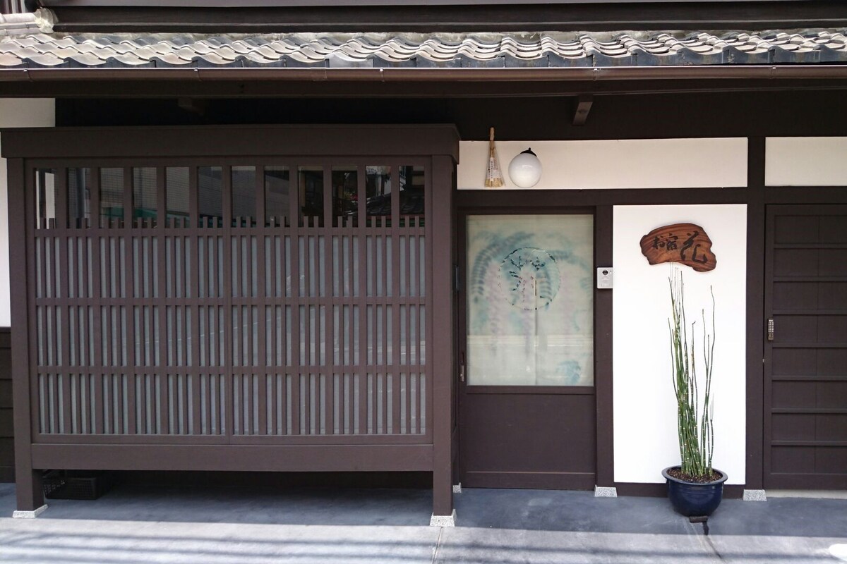 A traditional Japanese building with a sliding door, a small potted plant, and a wooden plaque with Japanese characters.
