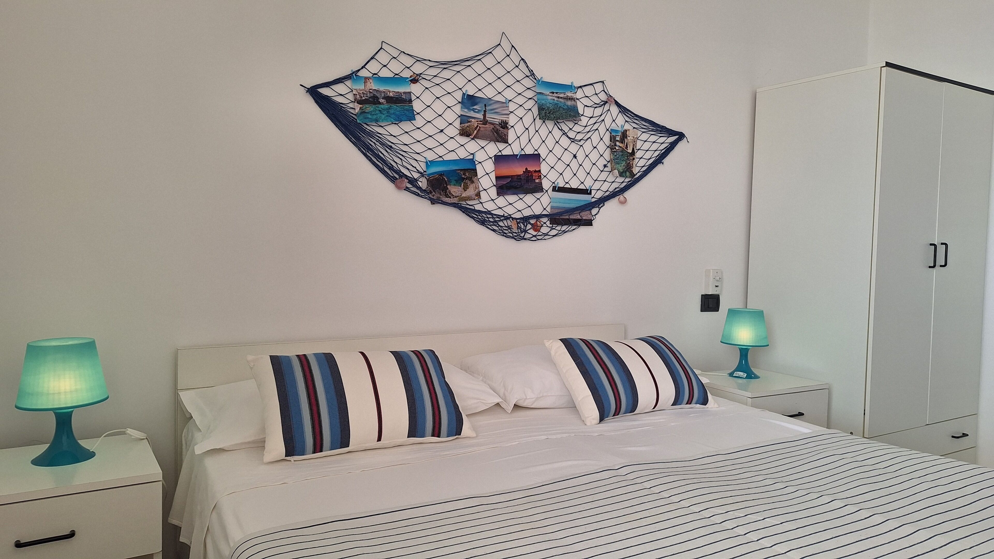 A neatly made bed with striped bedding, a wall-mounted photo collage, bedside lamps, and a wardrobe.